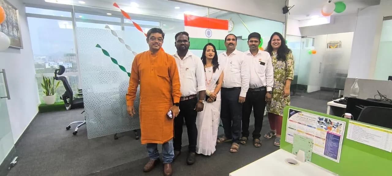 KIPL colleagues dressed in white beside the national flag on Independence Day