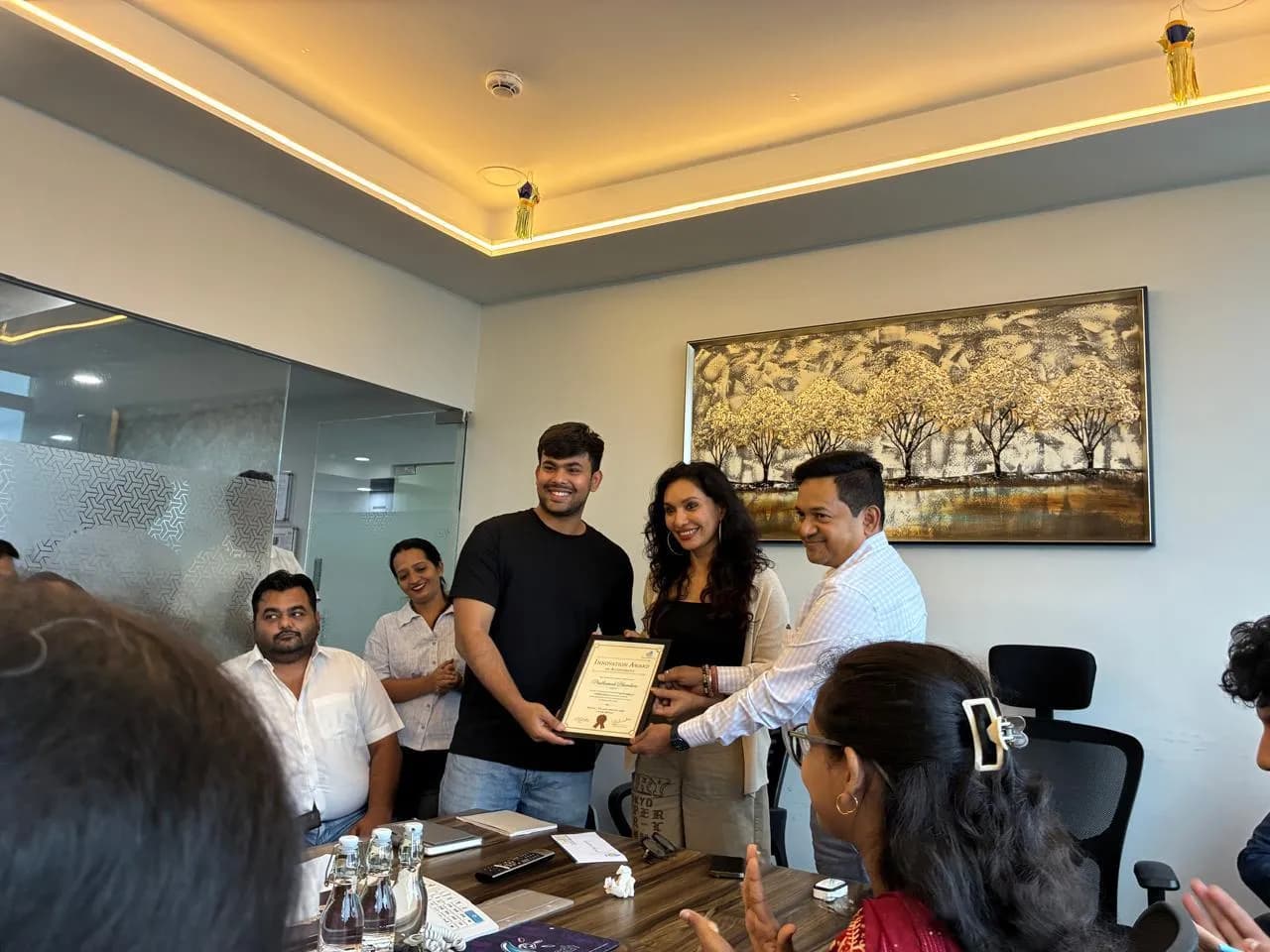 A certificate being handed to a KIPL colleague across a meeting-room table