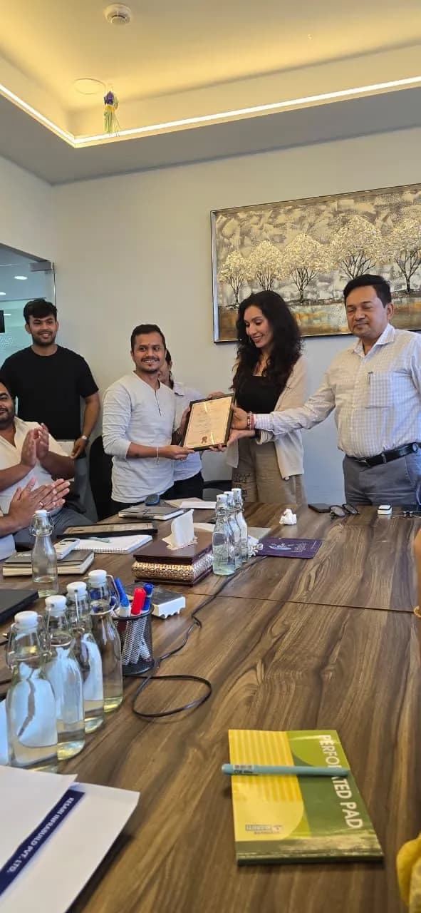 A certificate being handed to a KIPL colleague across a meeting-room table