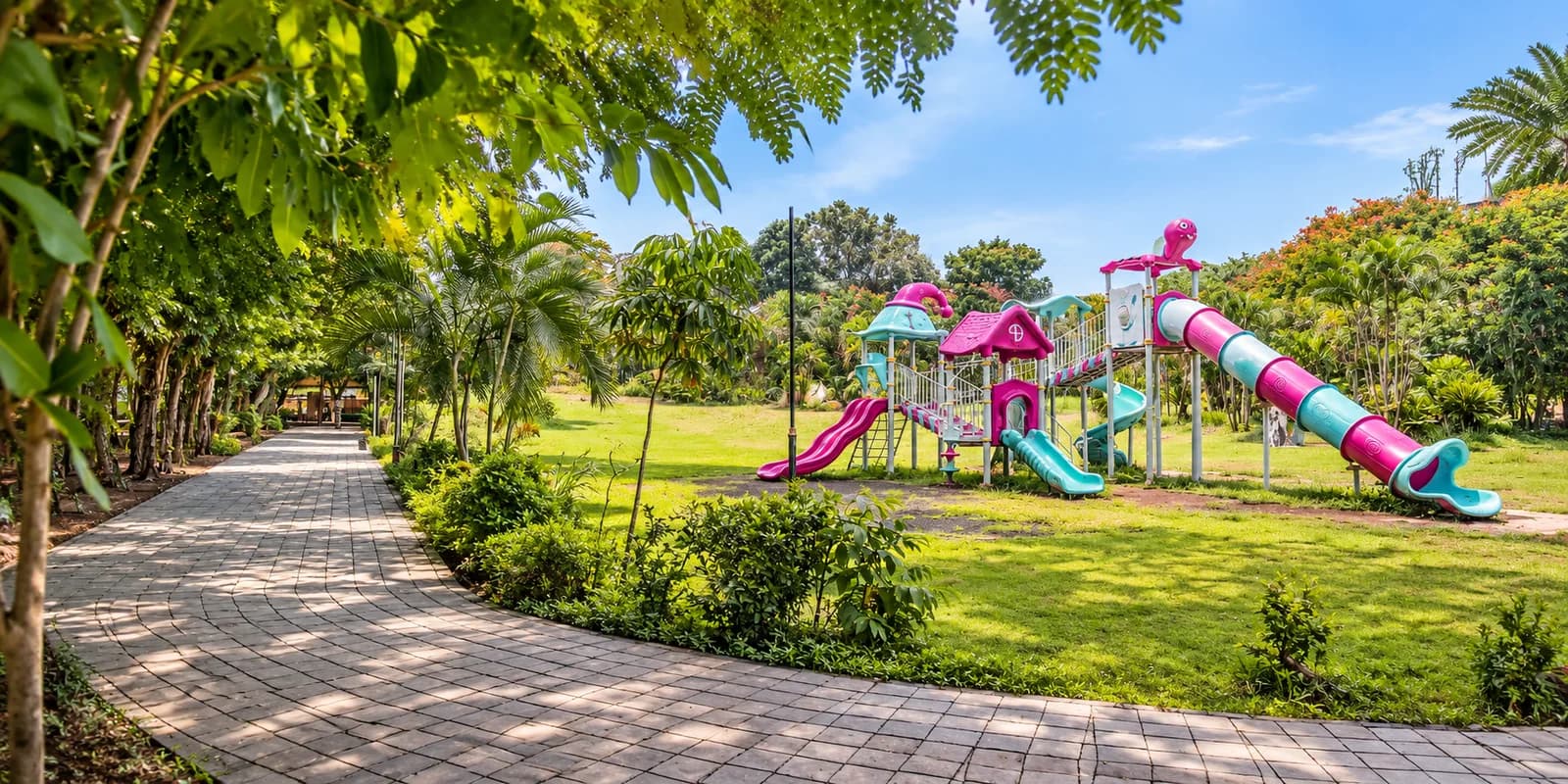 A maintained public garden at Kalamboli: mown lawn, clipped shrub beds and a flowering hedge beside a paved walk, with play equipment on the grass